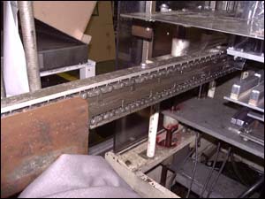 Figure 17. Guard chain rails to prevent access. For illustrative purposes only, the guard has been removed to better see the hazard associated with the pins on the spiked chain and sprocket mechanism used to feed the plastic roll stock through the different stations of the thermoforming machine.
