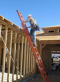 Construction worker on a portable ladder at proper angle against building under construction